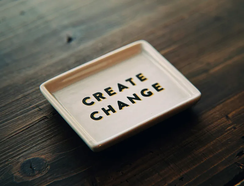 A small rectangular tray with the words "CREATE CHANGE" printed in black letters on a white background.