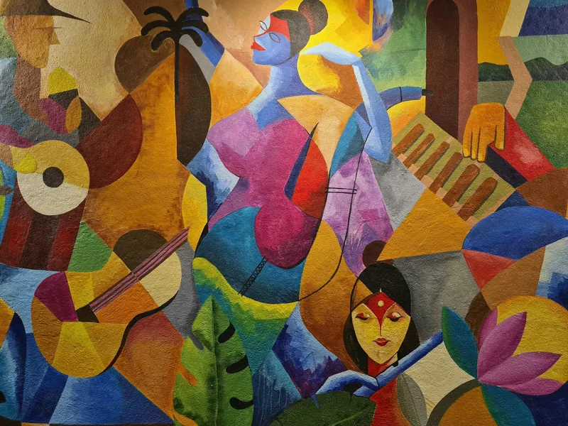 A colorful abstract mural featuring stylized human figures, musical instruments, flowers, and geometric shapes in vibrant colors.